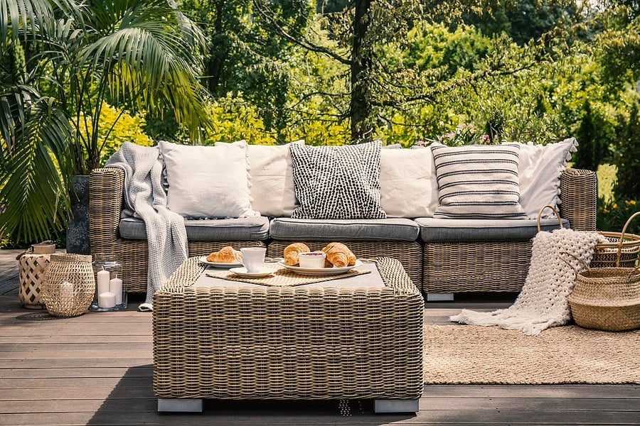 Patterned pillow on rattan chair next to sofa on terrace with rug in the garden. Real photo