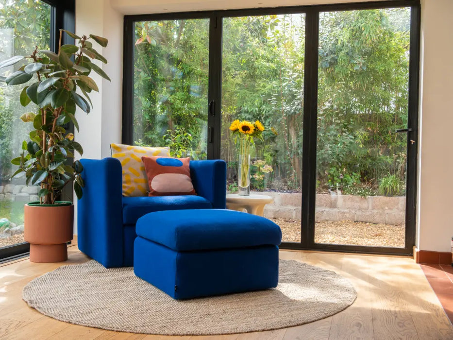 Photo By Lucy | Blue armchair and ottoman in a room with large windows and greenery outside