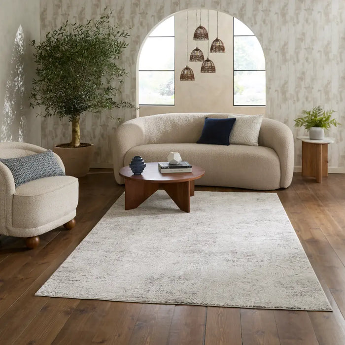 A large, rectangular area rug in a textured off-white/cream shag style, styled in a modern living room setting with a beige bouclé sofa, wooden coffee table, and dark wood floors.