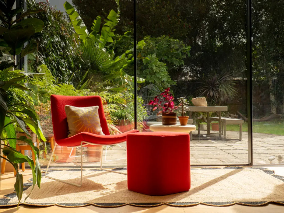 Photo by David Y | Red chair and ottoman on a patio with plants and a glass door in the background On a scalloped rug
