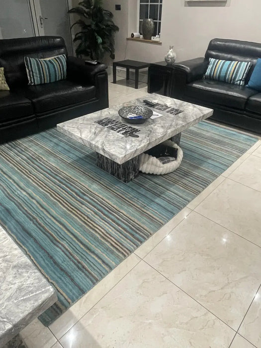 Photo By Musrat H. | Living room with black leather sofas, marble coffee table, and striped carter teal rug.