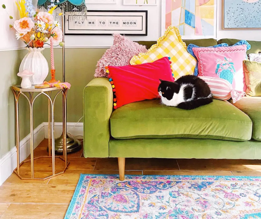 Photo By @lilyswatercolours | Green sofa with colorful pillows and a cat, surrounded by decorative items in a room.